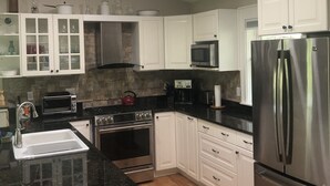 Una cocina moderna con armarios blancos, electrodomésticos de acero inoxidable, encimera de granito negro y suelo de madera.