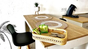 Une cuisine avec un plan de travail en bois, une chaise noire, un set de table en fibres tressées, une petite plante en pot et un plateau contenant des sacs verts.