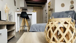 Une chambre moderne avec un plancher en bois, un lit recouvert d’une couvre-lit grise à motifs, une chaise noire, une table de chevet en bois et un panier tressé décoratif.
