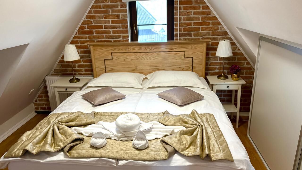 Ein ordentlich bezogenes Bett mit Kissen, Decke und Hut in einem Zimmer mit Backsteinwänden und einem hölzernen Kopfteil.
