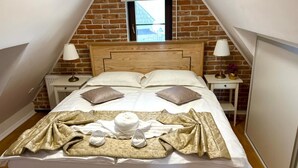A neatly made bed with pillows, a blanket, and a hat in a room with brick walls and a wooden headboard. - Dvosobni suite u potkrovlju (Plitvica Selo)