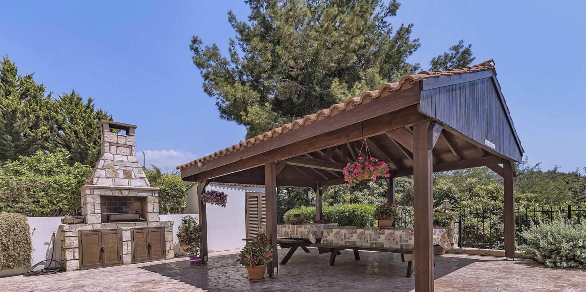 Een buitenkeuken van natuursteen met schoorsteen, een overdekte patio met pergola en potplanten.
