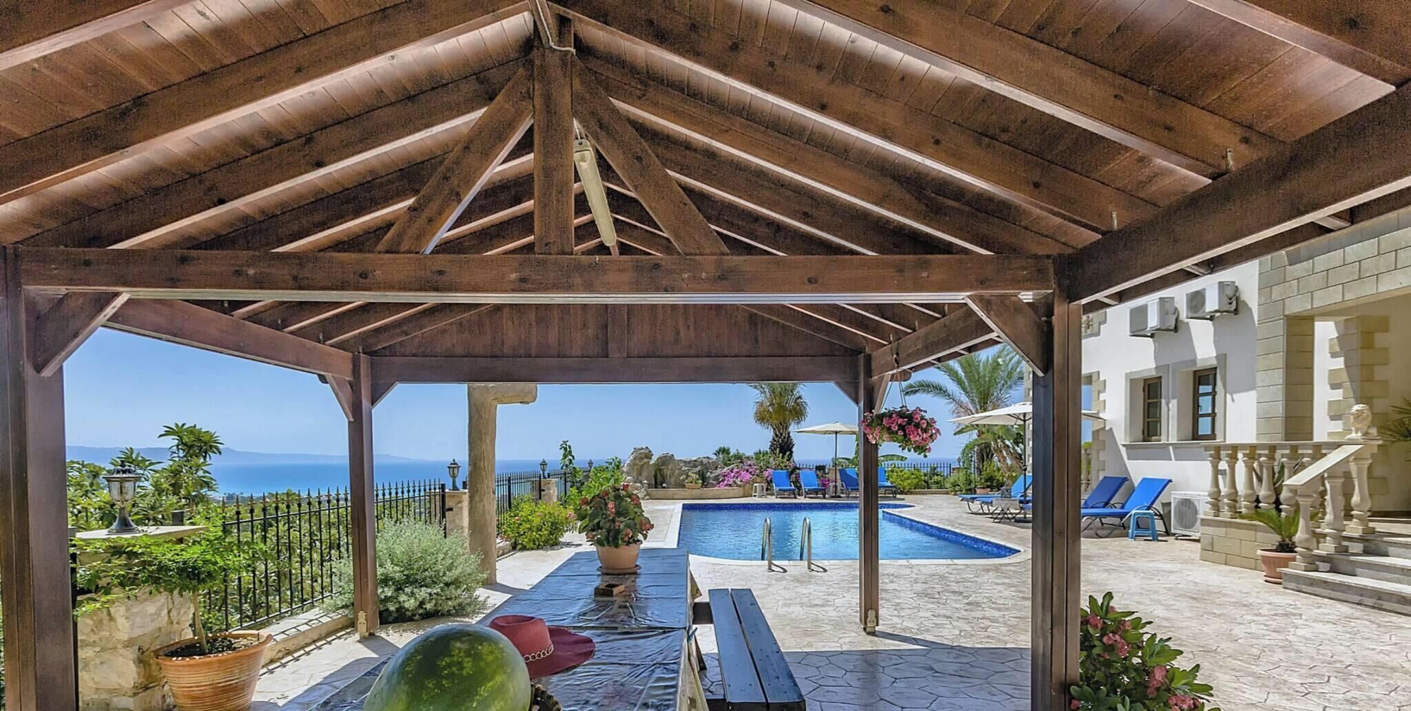 A covered outdoor area with a pool, lounge chairs, and a view of the sea.