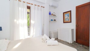 Um quarto com uma cama, uma porta de madeira, uma janela com cortinas, um radiador e uma prateleira com objetos decorativos.