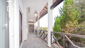 Um corredor externo coberto com piso de pedra, paredes brancas e grade de metal.