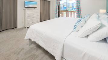 Een slaapkamer met een bed, een televisie op een dressoir, en een balkon met gordijnen.