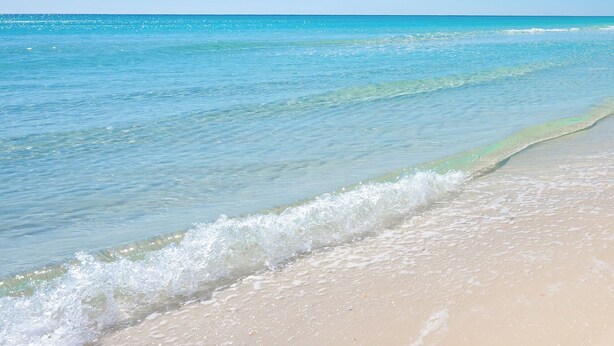 A beach with clear blue water and a sandy shore.