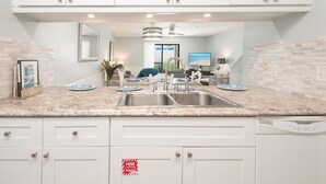 A modern kitchen with white cabinets, a double sink, and a dining area with a TV and seating.