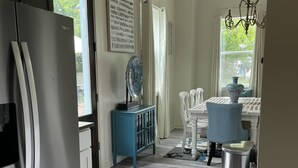 A modern kitchen with a refrigerator, a dining area with a table and chairs, and a window with curtains. - Gorgeous beach view, private balcony suites (Biloxi)