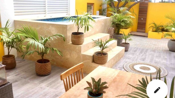 A patio area with a pool, potted plants, a wooden table, and a chair.