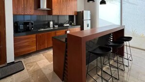 A modern kitchen with wooden cabinets, a central island with bar stools, and pendant lighting. - Casa Montes de Amé, gran ubicación y comodidad (Mérida)