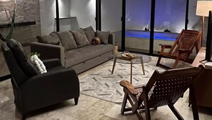 A modern living room with a sofa, a chair, a coffee table, and a view of a beach through large windows. - Casa Montes de Amé, gran ubicación y comodidad (Mérida)
