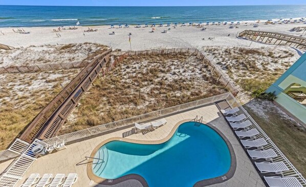 A beach resort with a swimming pool, beach chairs, and a wooden deck.
