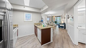 A modern kitchen with a central island, white cabinetry, and a stainless steel refrigerator. - Harbour Place 310 (Orange Beach)