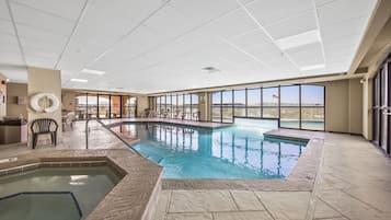 An indoor swimming pool with a hot tub, large windows, and a view of a distant landscape.
