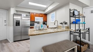 A modern kitchen with stainless steel appliances, wooden cabinets, and a granite countertop. - Harbour Place 310 (Orange Beach)