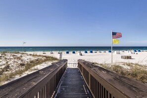 A wooden boardwalk leading to a beach with tents and a flag.