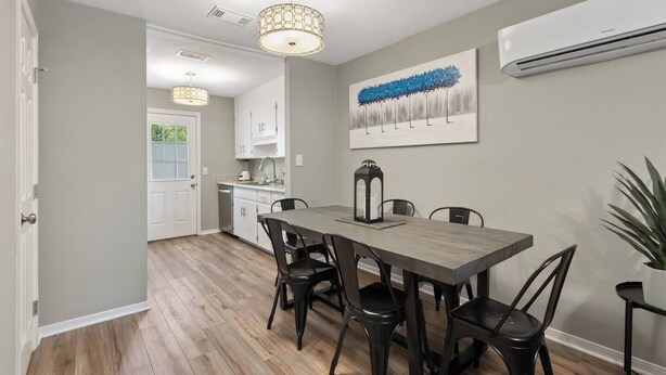 A dining area with a wooden table and chairs, a pendant light, and a painting on the wall.