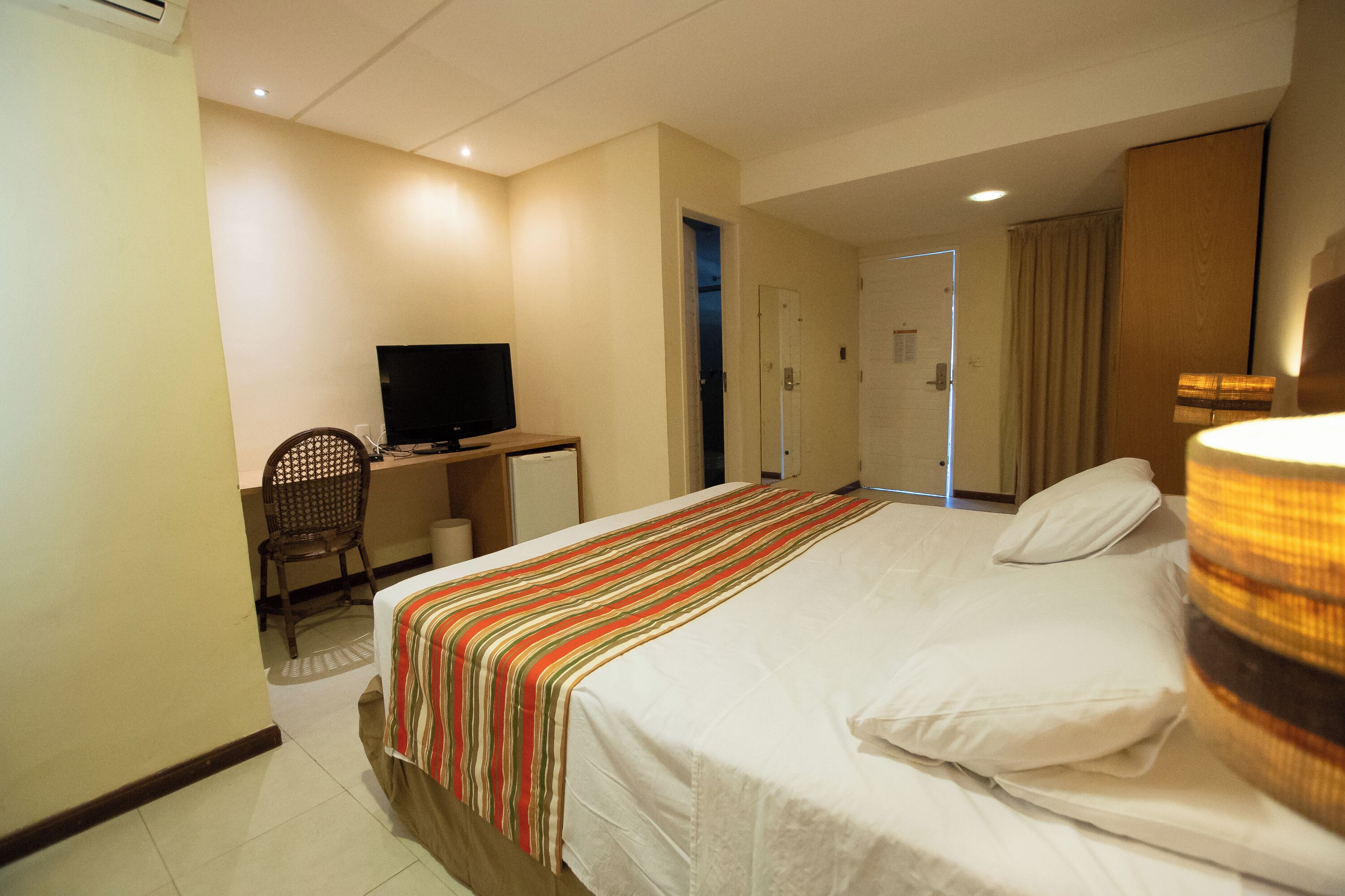 A hotel room with a bed, a desk with a television, a chair, and a wardrobe.
