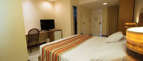 A hotel room with a bed, a desk with a television, a chair, and a wardrobe.