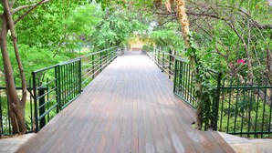A wooden pathway with metal railings, surrounded by lush greenery and trees. - Hotel Villaoeste (Mossoro)