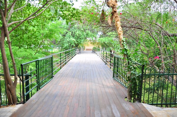 A wooden pathway with metal railings, surrounded by lush greenery and trees. - Hotel Villaoeste (Mossoro)