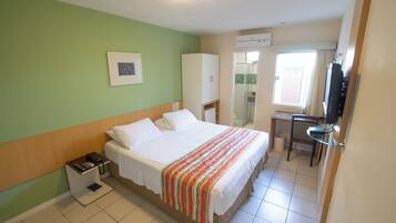 Una habitación de hotel con cama, escritorio, armario y televisor.