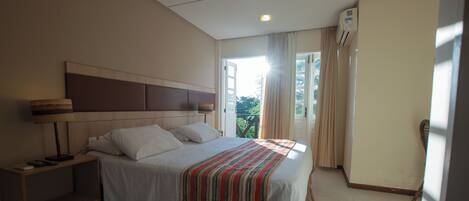 A hotel room with a bed, bedside table, and a view of the outdoors.