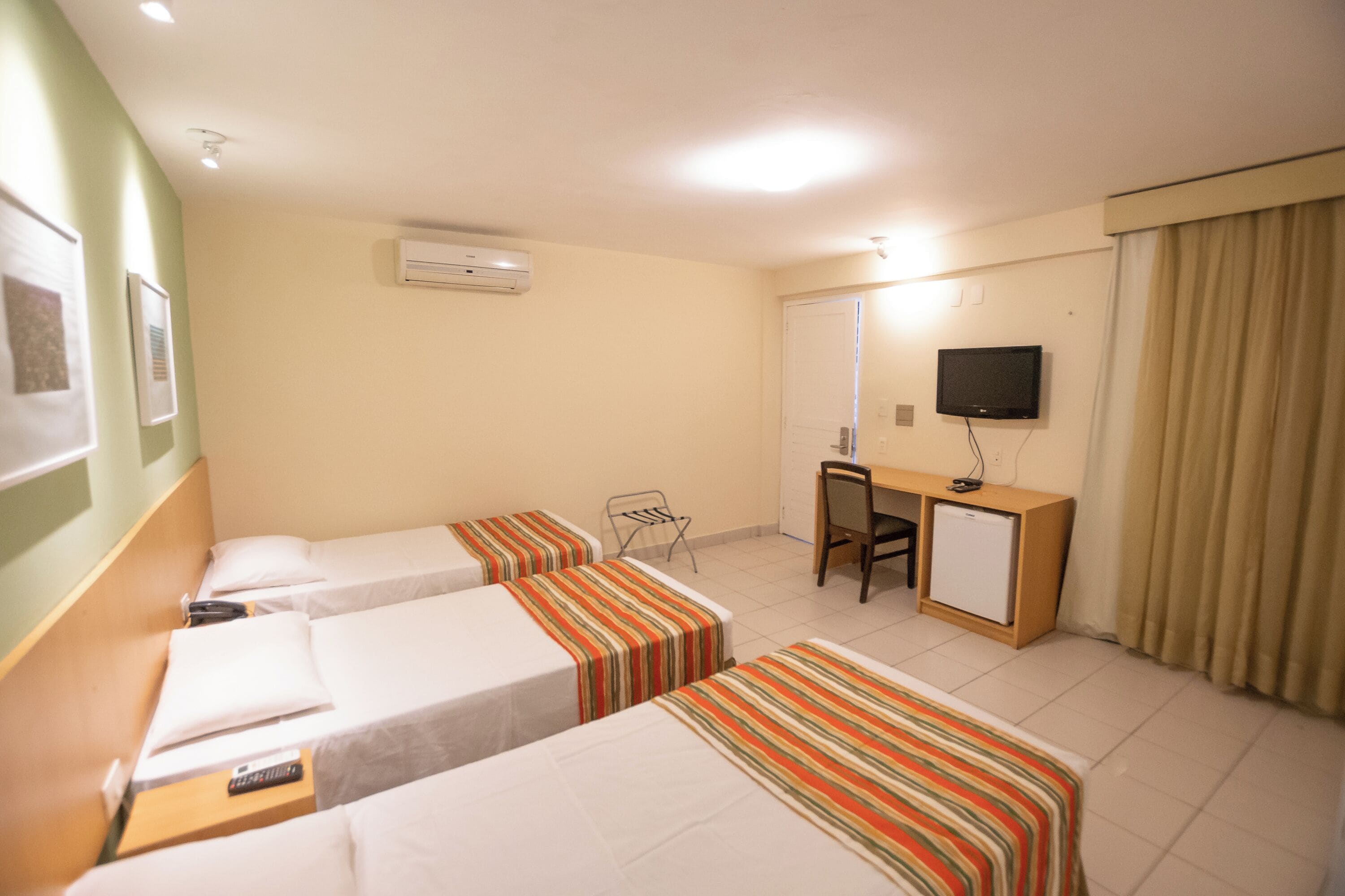 Une chambre d’hôtel avec deux lits simples, un bureau avec une chaise, une télévision et un appareil de climatisation.