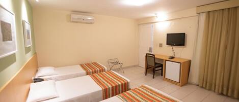 A hotel room with two single beds, a desk with a chair, a television, and an air conditioning unit.