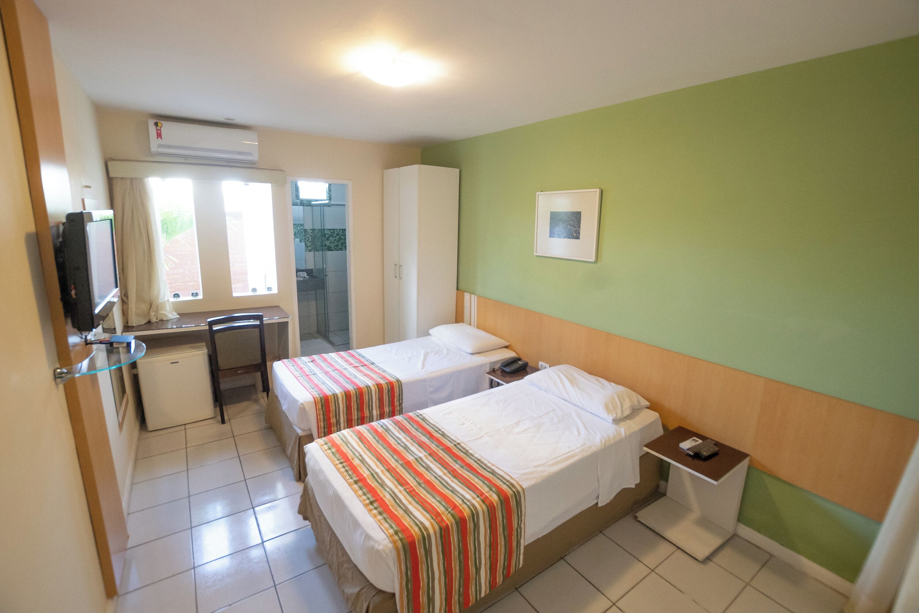 A hotel room with two beds, a desk, a chair, a small refrigerator, and a television.