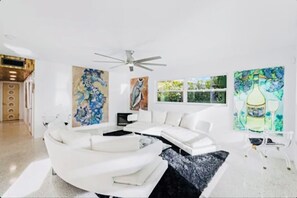 Een moderne woonkamer met een witte bank, een plafondventilator en abstracte schilderijen aan de wanden.