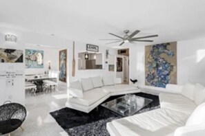 A modern living room with a white sectional sofa, a glass coffee table, and abstract art on the walls.
