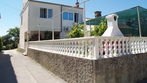 A two-story house with a balcony, a white fence, and a green netting structure. - Spacious Holiday House Domenico (Preko)