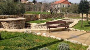 A stone bench in a landscaped garden with a stone wall and a pathway. - Spacious Holiday House Domenico (Preko)