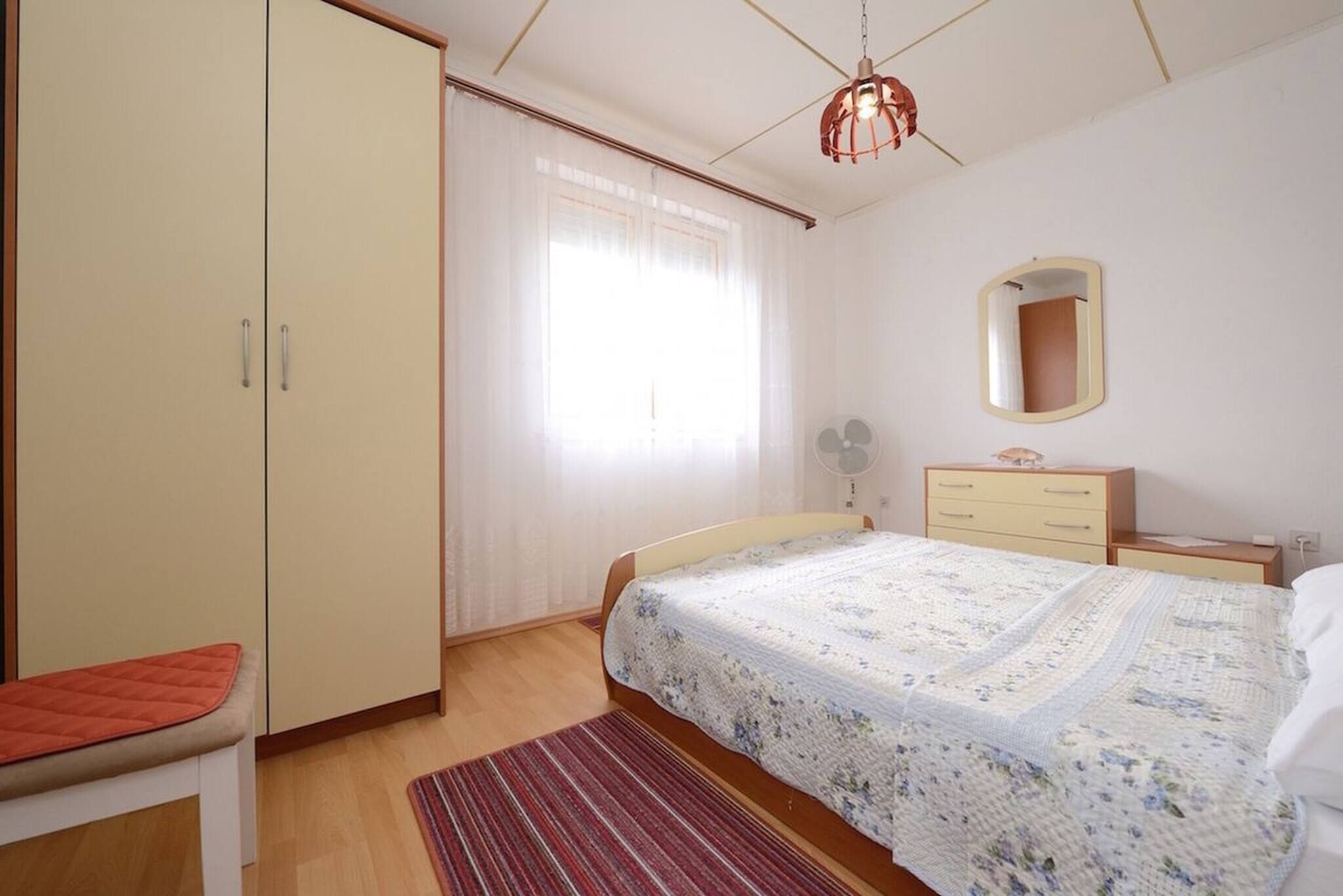 Une chambre à coucher comprenant un lit, une armoire, une table de chevet, un miroir et une fenêtre avec des rideaux.