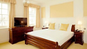 A hotel room with a large bed, a TV, a dresser, and a nightstand with a lamp. - Kings Arms Bicester (Bicester)