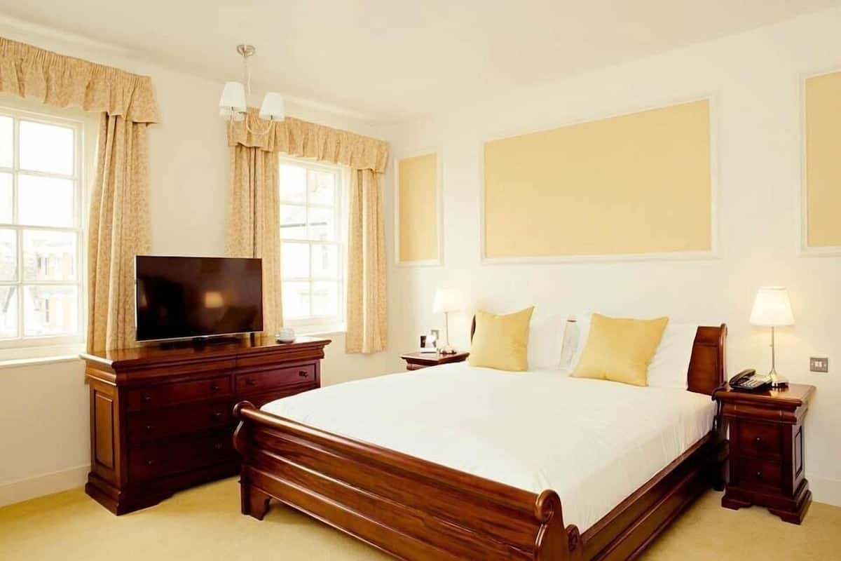 A hotel room with a large bed, a TV, a dresser, and a nightstand with a lamp.