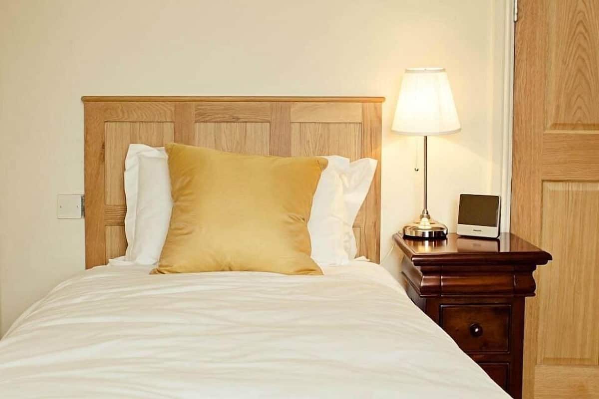A neatly made bed with a wooden headboard, a bedside lamp, and a small bedside table with a screen.