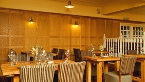 A restaurant with wooden paneled walls, striped upholstered chairs, and tables set with wine glasses and cutlery. - Kings Arms Bicester (Bicester)