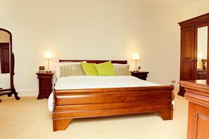 Una cama de madera tradicional con cabecera, dos mesitas de noche con lámparas y un espejo de cuerpo entero.