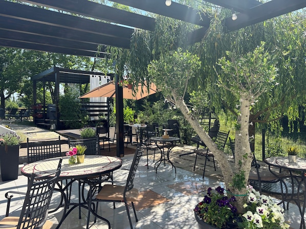 Un patio al aire libre con mesas y sillas redondas, una pérgola y una parrilla.