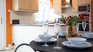 A kitchen with wooden cabinets, a microwave, and a sink. There are two white bowls with "DINNER" and "SUPPER" written on them, and two wine glasses on a table. - Hurley House (Cheadle)