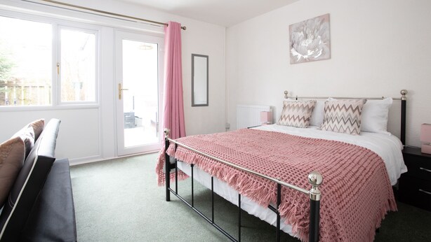 A bedroom with a bed, a bench, a window with a curtain, and a wall-mounted picture. - Hurley House (Cheadle)