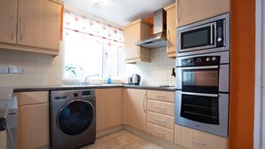 A kitchen with a washing machine, microwave, oven, and wooden cabinets. - Hurley House (Cheadle)