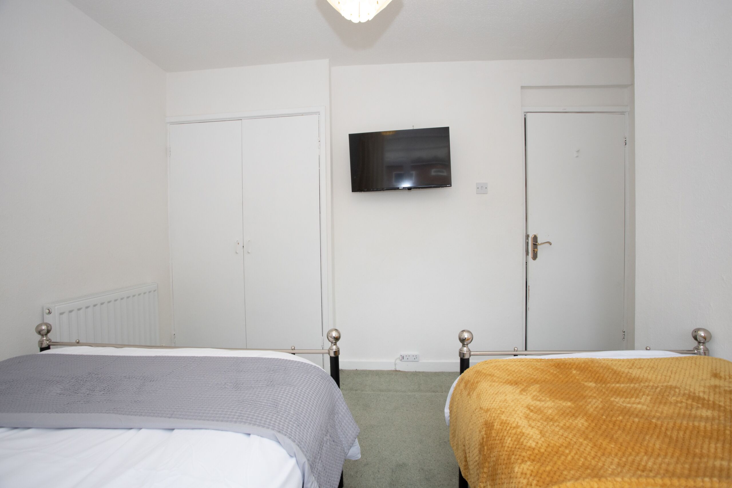 A bedroom with two beds, a television on the wall, and two doors.