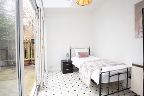 A bedroom with a bed, a nightstand, a radiator, and a window. - Hurley House (Cheadle)
