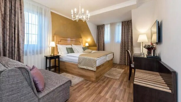 Ein Hotelzimmer mit einem hölzernen Bett, einer Couch, einem Schreibtisch und einem Chandelier.