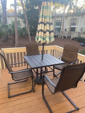 A deck with a table and four chairs, an umbrella, and a building in the background. - Hilton Head · Beautiful Hilton Head Condo across from the beach! (Hilton Head)