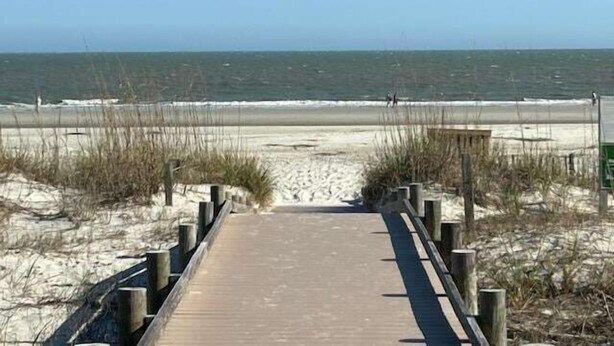 Un muelle de madera que conduce a una playa arenosa con el océano al fondo.